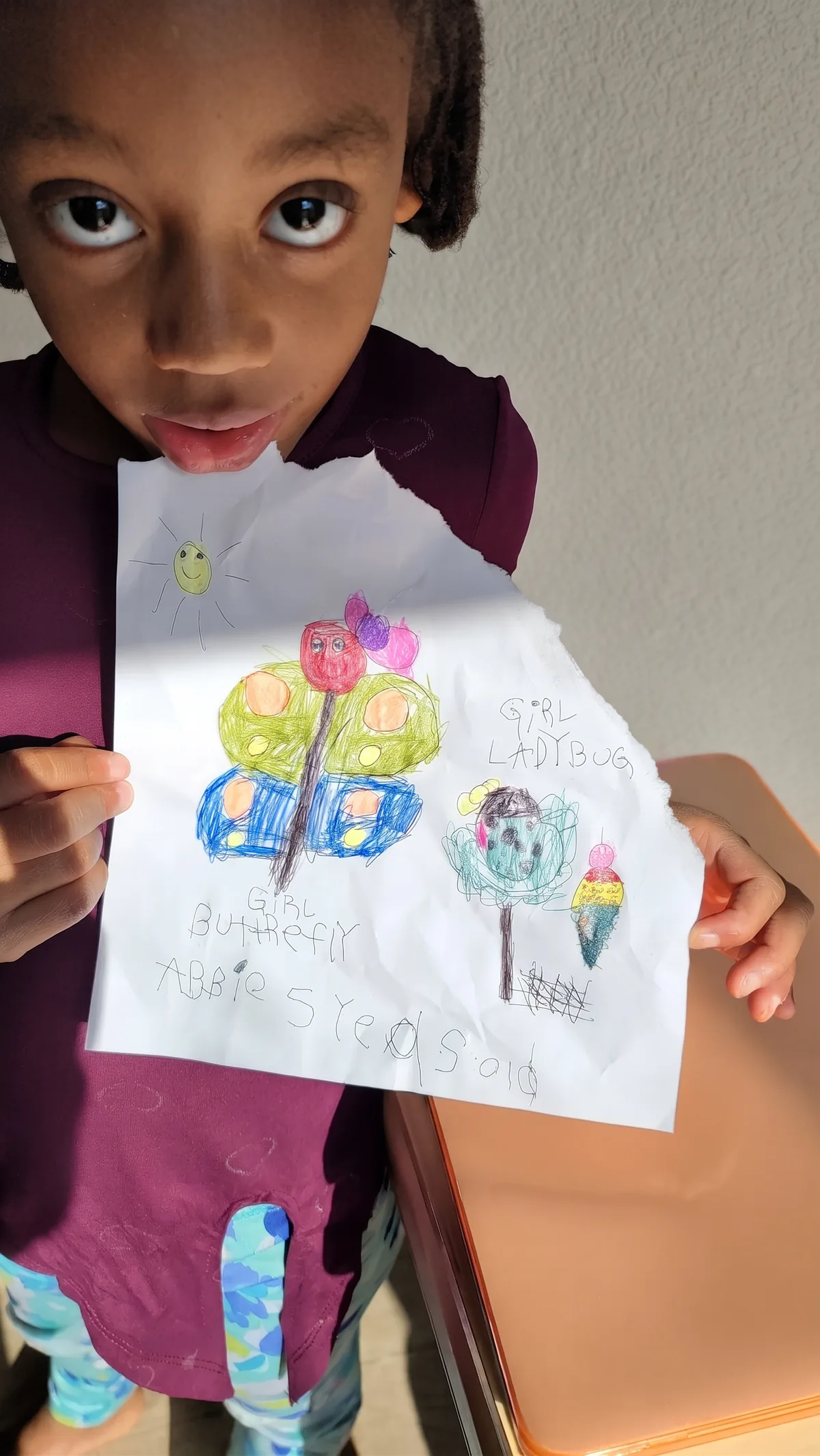 Abbie at five, holding her crayon drawing of "Girl Butterfly" and "Girl Ladybug"
