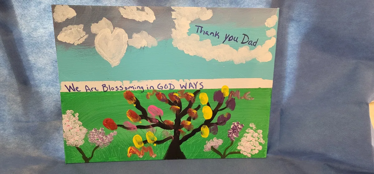 Acrylic painting of a tree with finger-painted leaves and the words "We are blossoming in GOD ways"