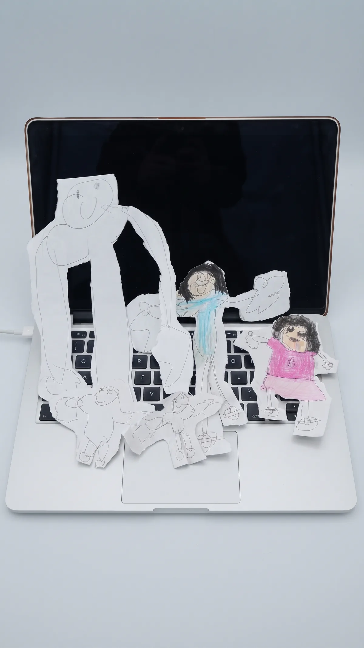 Hand-drawn paper figures of a family, cut out and arranged on a laptop