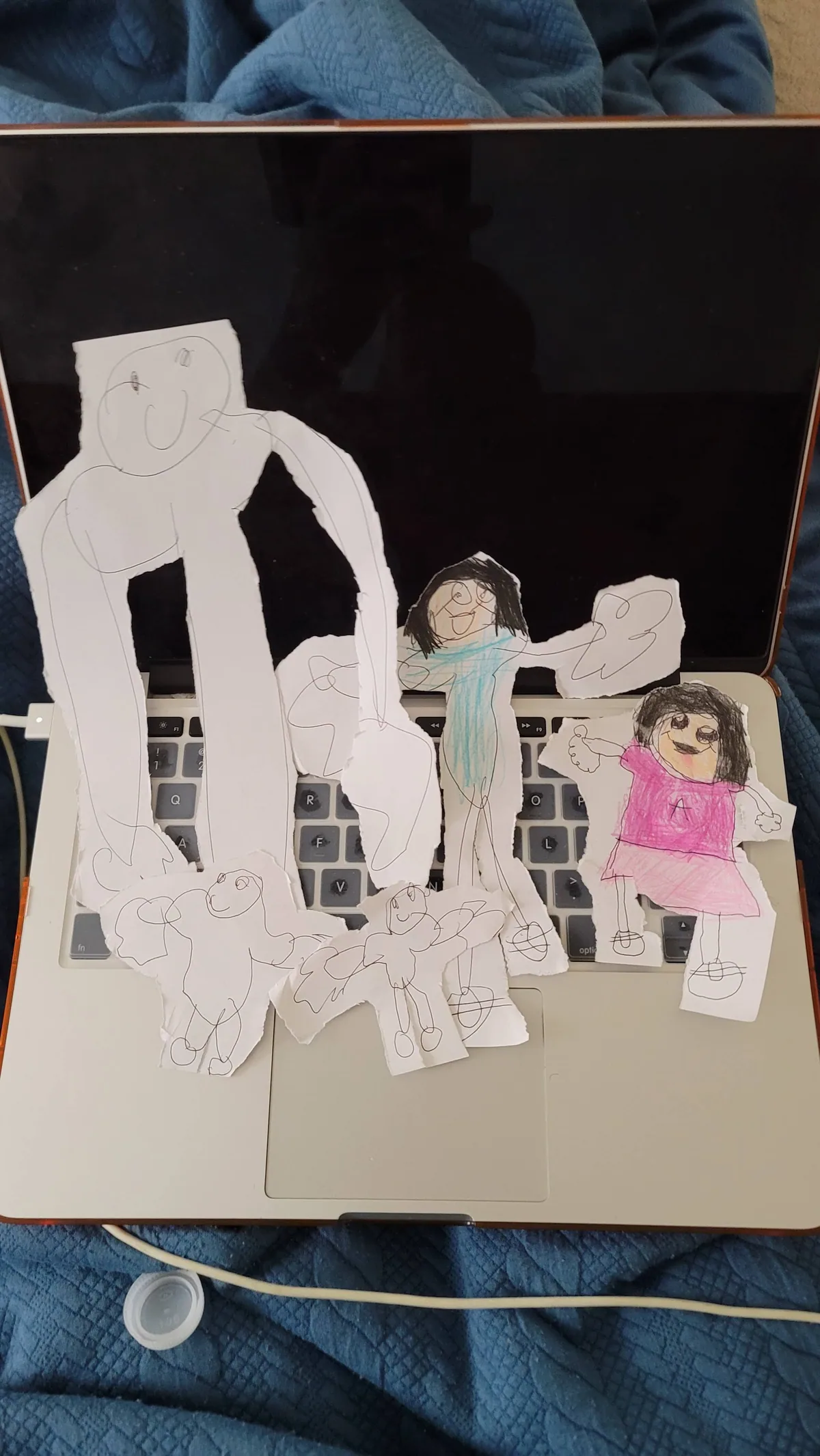Hand-drawn paper figures of a family, cut out and arranged on a laptop