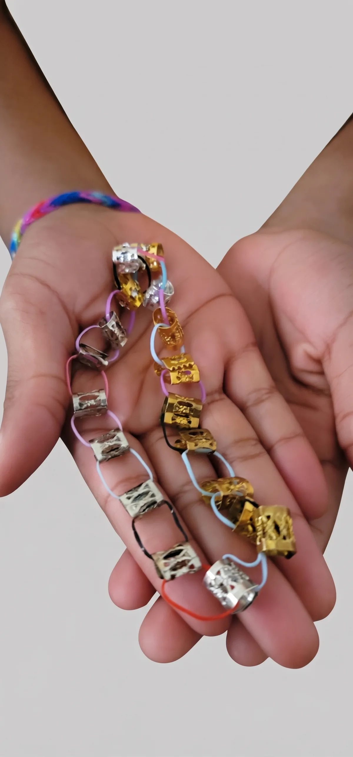 A child's hands holding decorative metallic bead-and-rubber-band bracelet