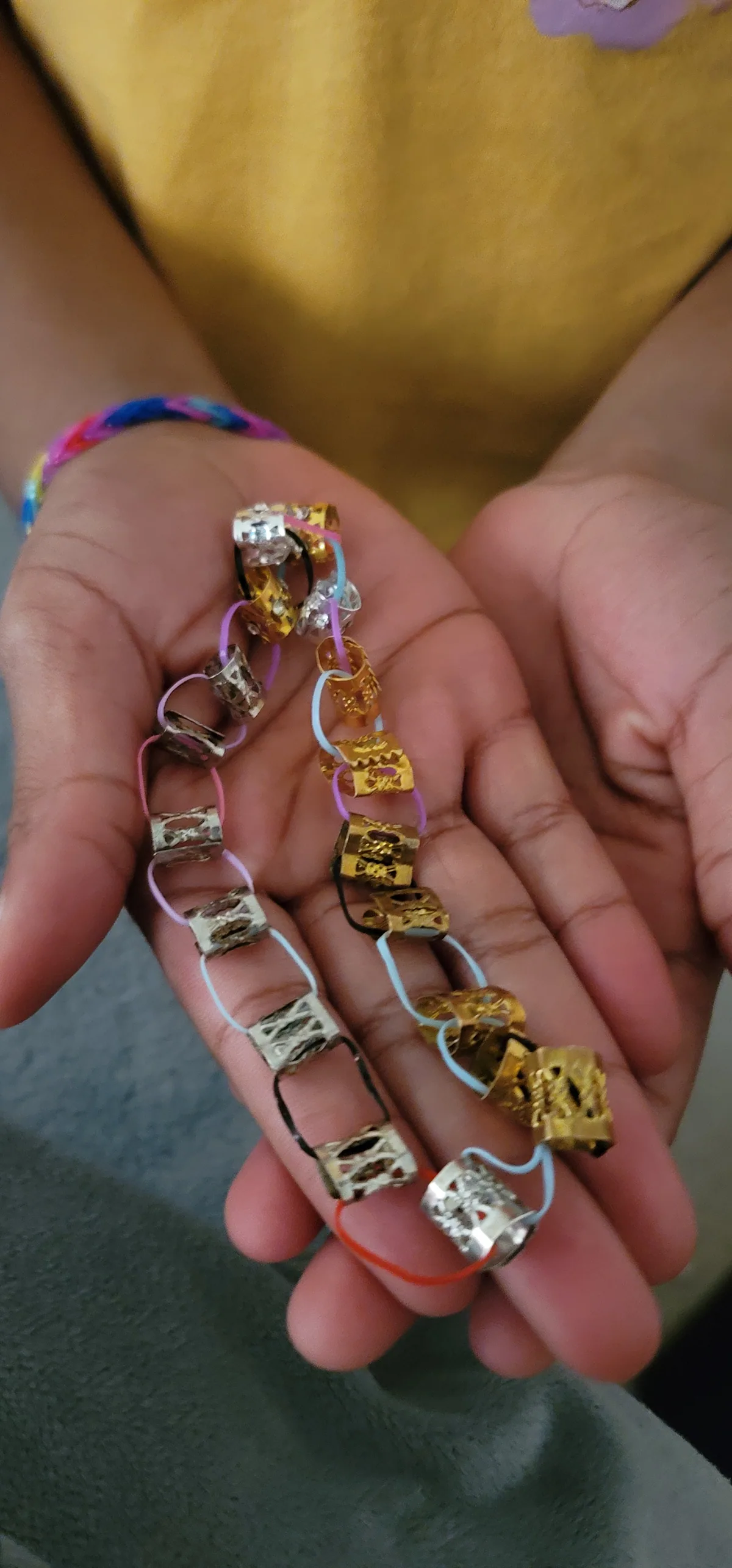 A child's hands holding decorative metallic bead-and-rubber-band bracelet