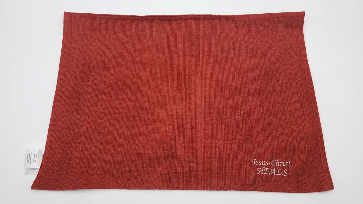 Red waffle-weave placemat with embroidered "Jesus-Christ Heals" in pale thread