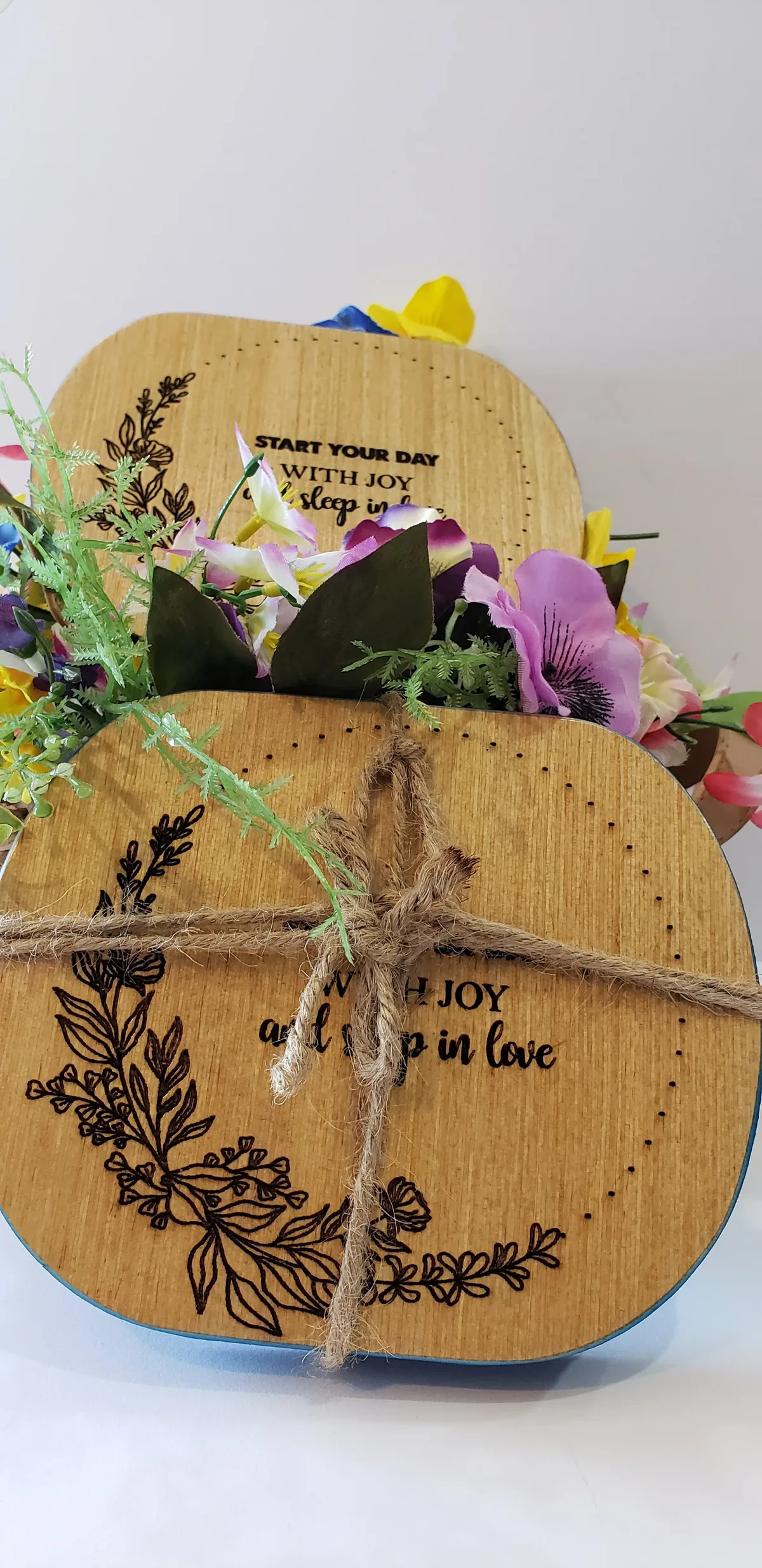 Two engraved wooden plaques "Start your day with joy" bound with twine, framed by flowers