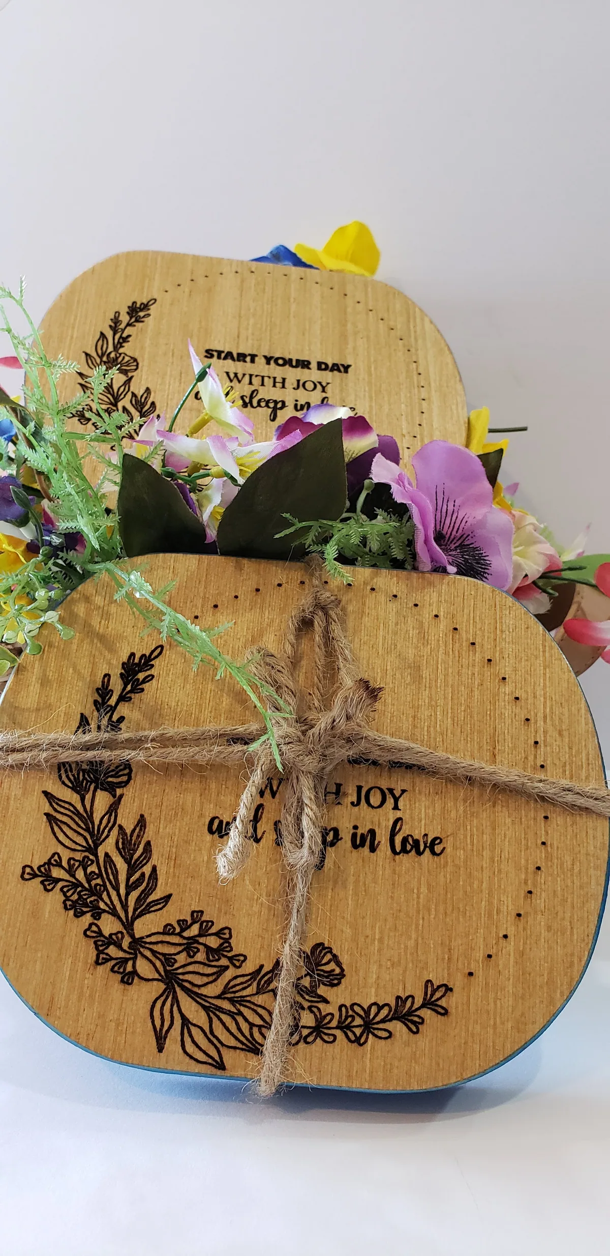 Two engraved wooden plaques "Start your day with joy" bound with twine, framed by flowers