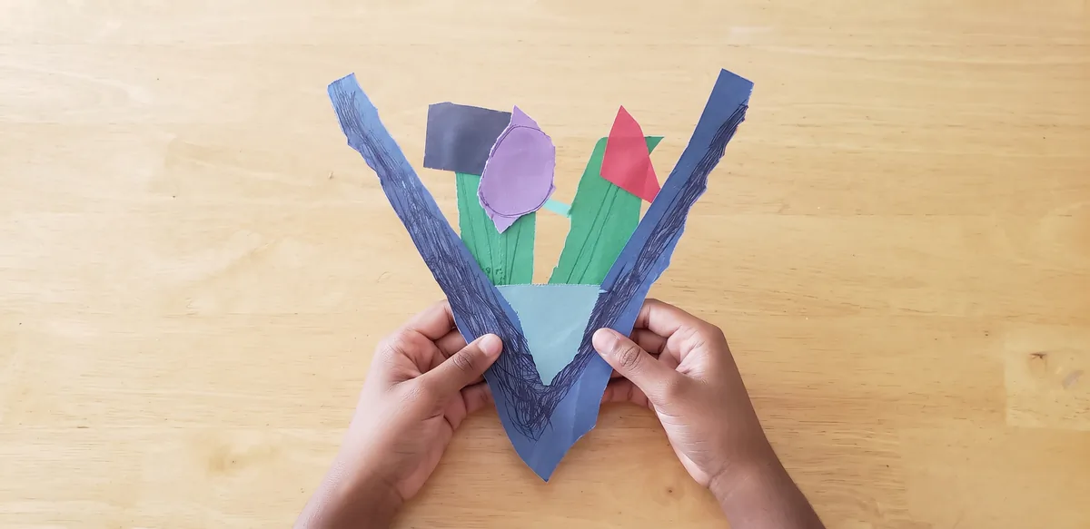 A child mid-collage at the workshop table, cutting and gluing coloured construction paper
