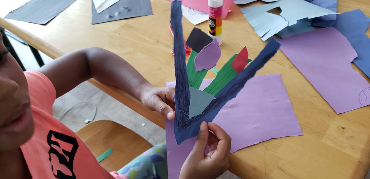 A child mid-collage at the workshop table, cutting and gluing coloured construction paper
