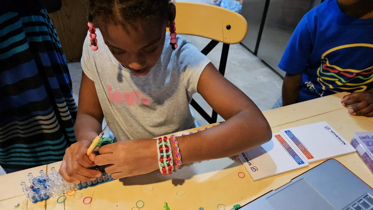 A girl with beaded braids weaving a rubber-band loom bracelet, multiple finished ones on her wrist