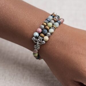 A Tri-Strings bracelet worn on a wrist, three wraps of stone and silver closed with a flower toggle